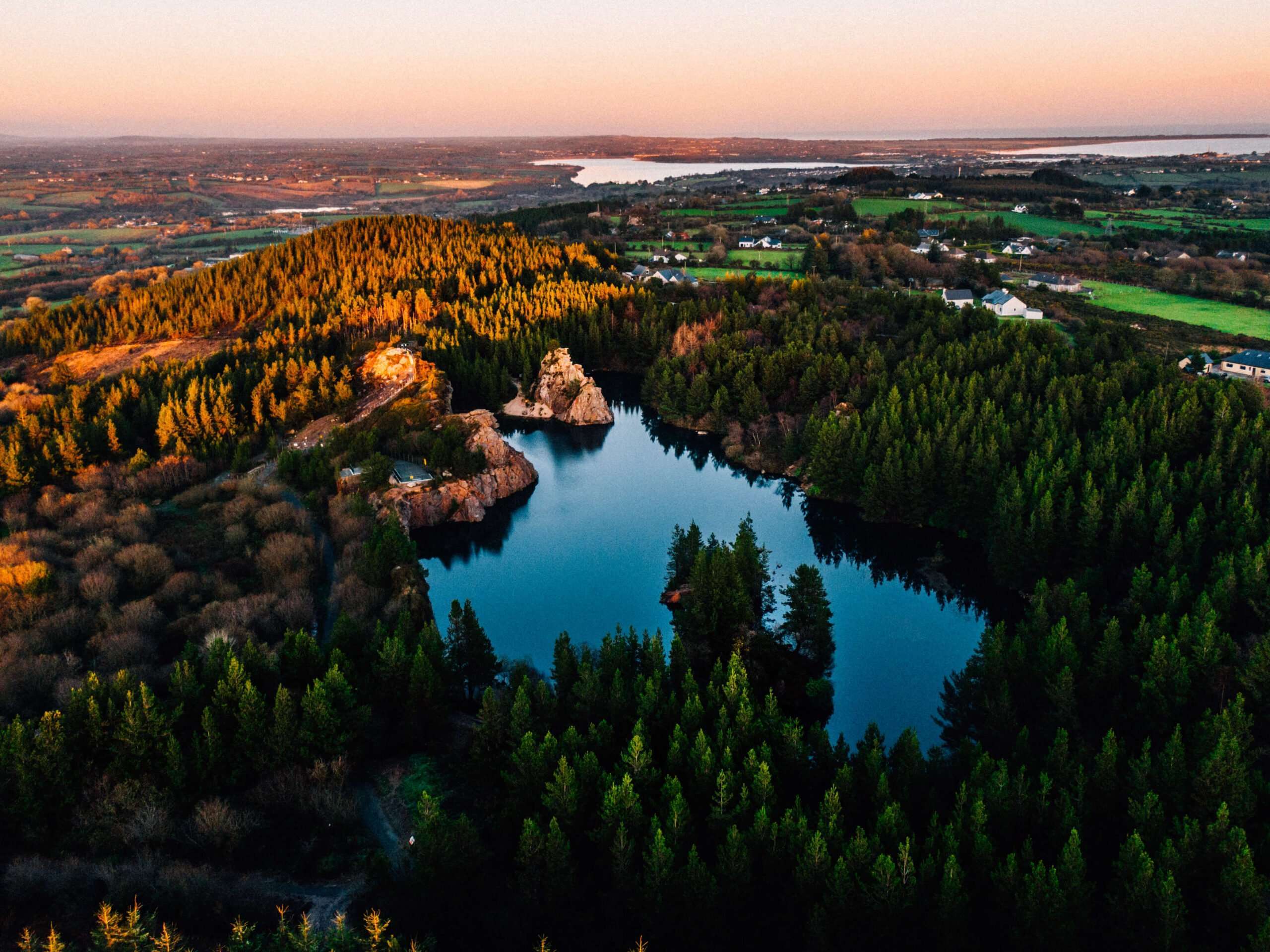 Aerial view of an Irish quarry lake surrounded by forestry at sunset